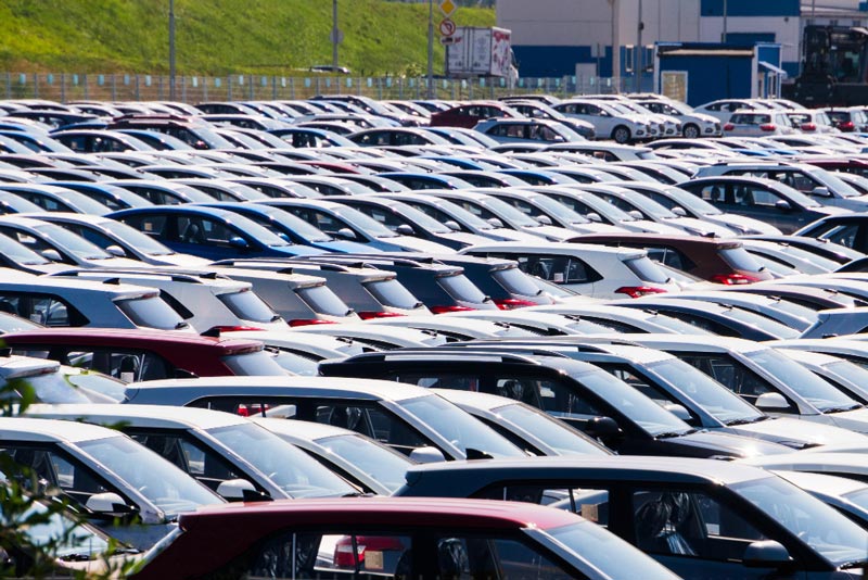 Ein dicht bepackter Parkplatz bei Gebrauchtwagen Ankauf Hamm ist mit Reihen geparkter Autos in verschiedenen Farben, hauptsächlich Weiß und Rot, unter einem sonnigen blauen Himmel gefüllt.